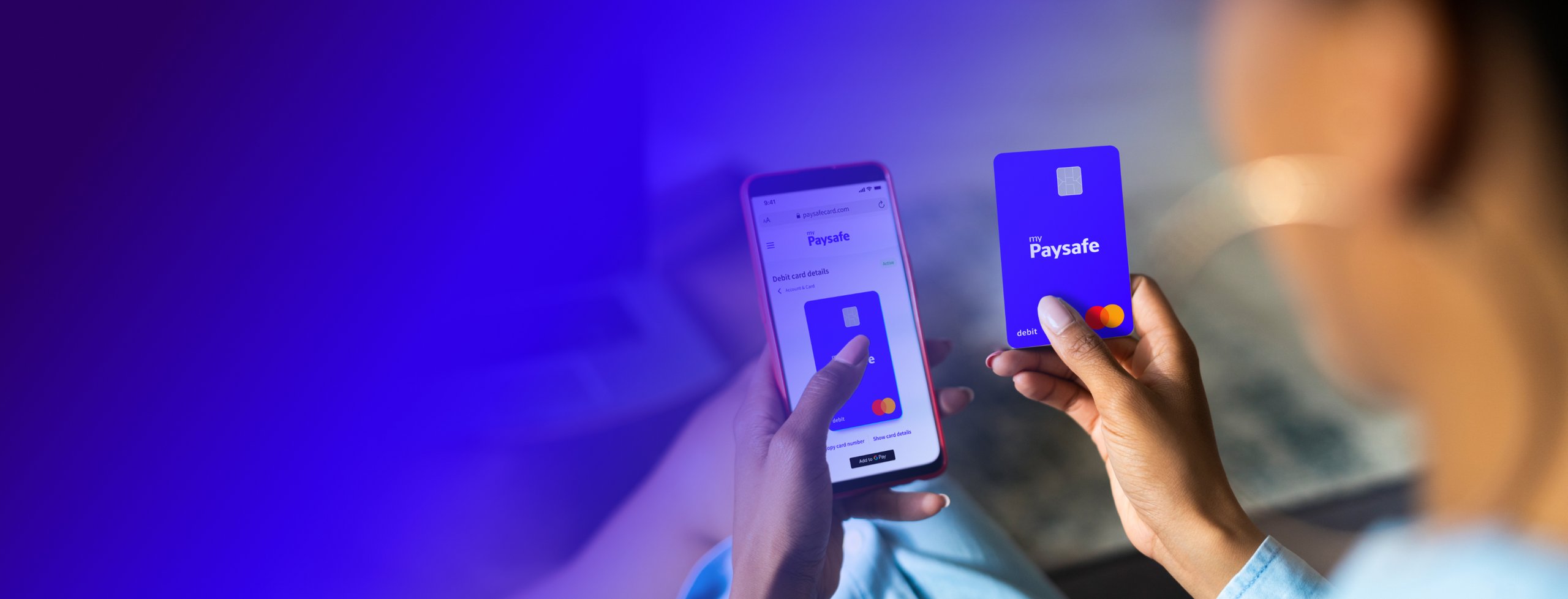 phone showing PaysafeCard application in the left hand and a Debit Mastercard in the right hand