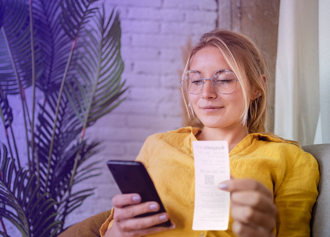 woman looking at a mobile phone and holding a PaysafeCard voucher in the other hand