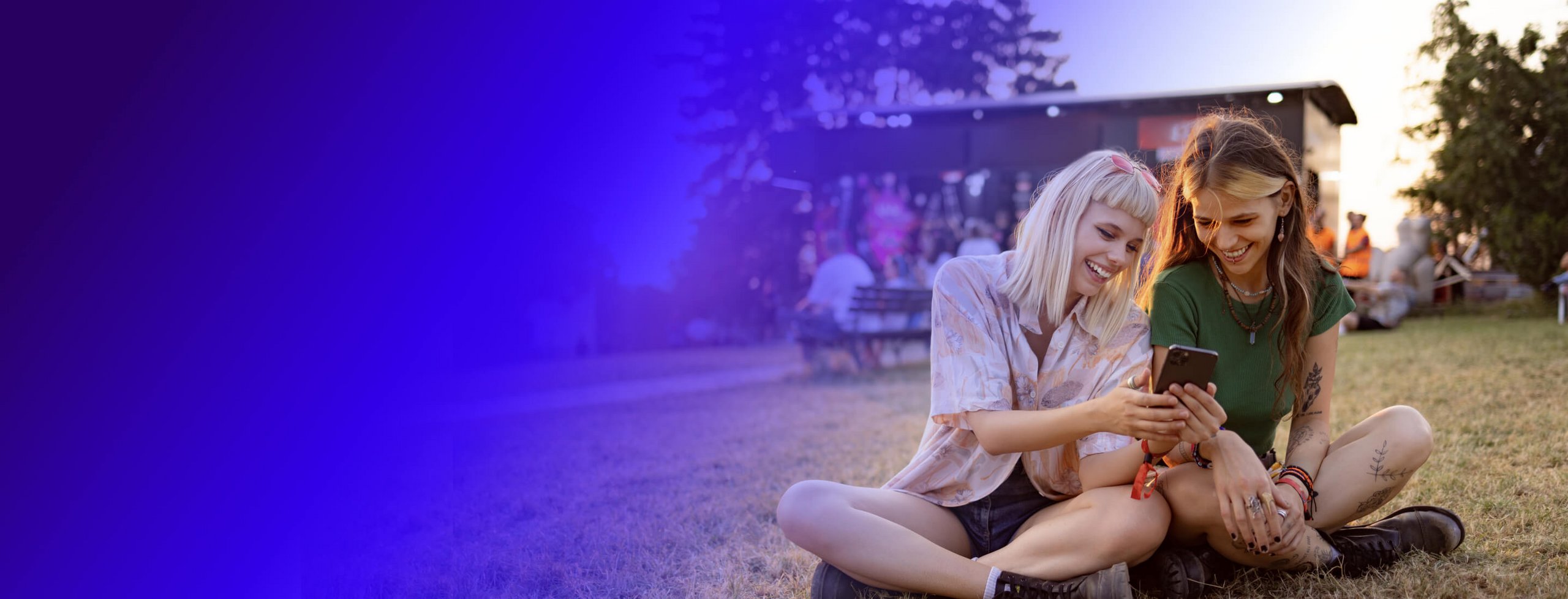Two happy girls laying in the grass and looking at their phone