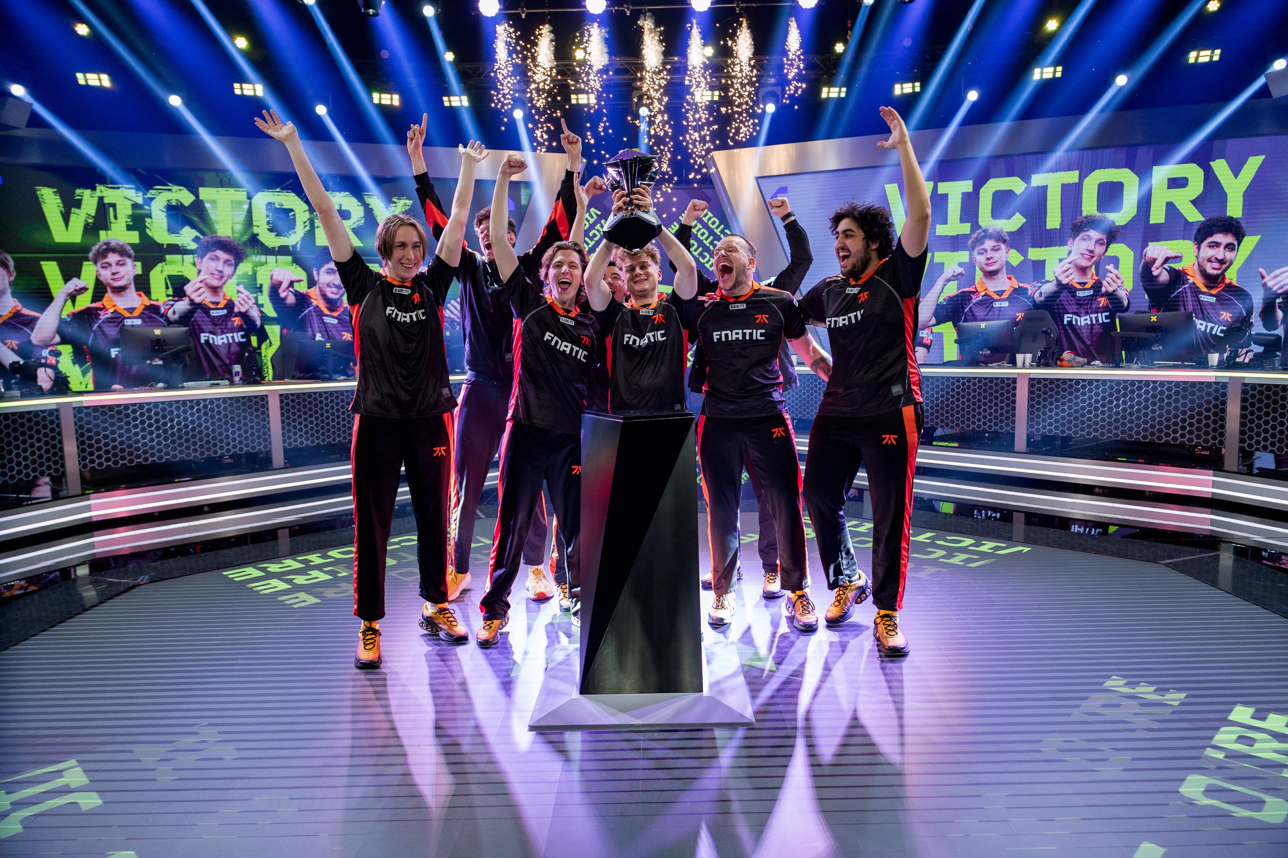 Fnatic celebrates on stage with trophy and confetti under “VICTORY” banner