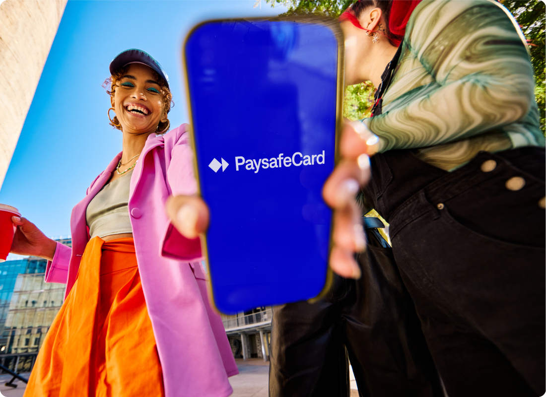 woman holding a phone showing the PaysafeCard logo to the screen and smiling 